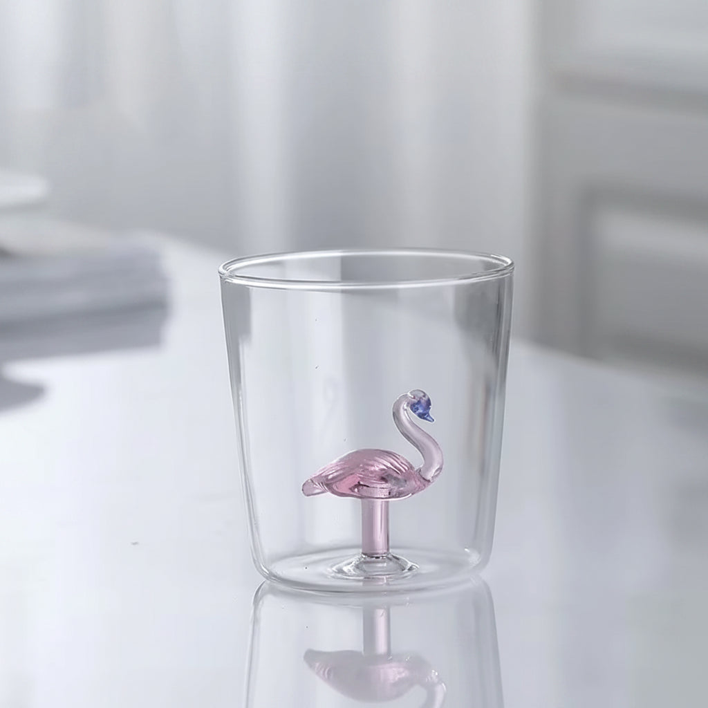 Clear glass tumbler with a pink flamingo drink valve on a white background