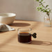 Glass mug with heart-shaped handle filled with dark liquid on a light surface.