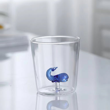 Clear glass cup with a blue whale-shaped object inside on a light background