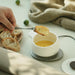 Person dipping bread into a cup of soup on a table with a beige cloth in the background